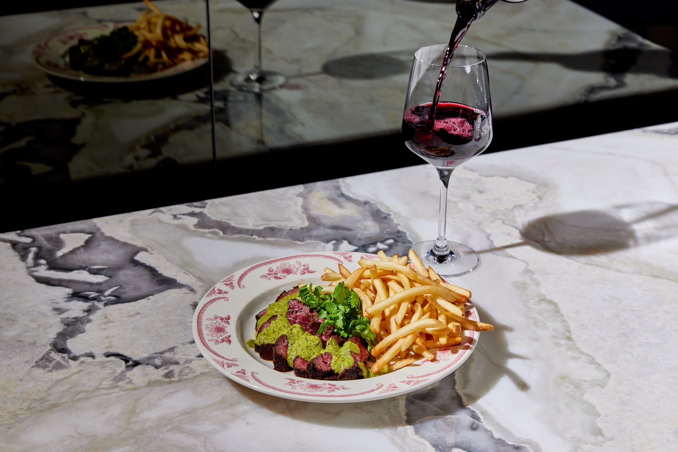 Dry-aged steak and fries with a glass of red wine on the marble bar at Sirrah